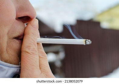 A woman smokes a cigarette on the street, close-up. A smoking cigar in the mouth.