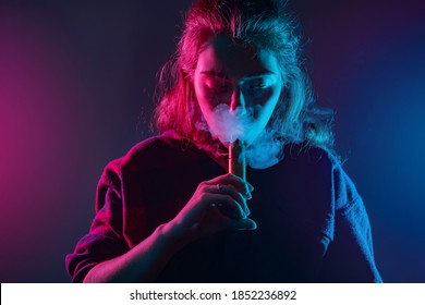Woman smokes a vape. Girl with an e-cig at the mouth. Smoking with a vape device. Woman inhales the smoke of a cigarette. Concept - a store for vaping devices. Sale of electronic cigarettes. Student
