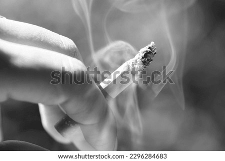 woman smoking a burning cigarette with smoke between her fingers on the street with a natural background copy space. Cigarette ending with white smoke. cigarette smoking consumable