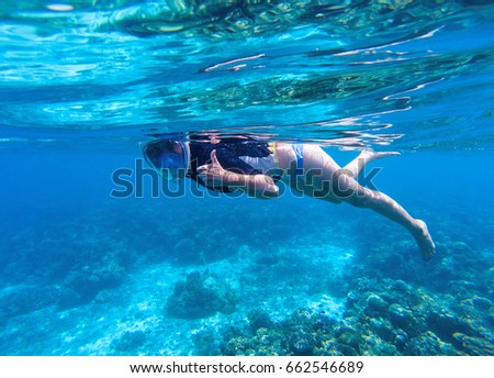 Woman snorkeling in blue water. Snorkel shows thumb in full face mask. Summer activity. Beautiful girl swims in sea. Underwater photo of oceanic landscape. Seaside adventure. Water sport in tropic sea
