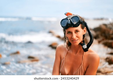 Woman with snorkeling gear smiles on rocky seashore. Attractive female ready for diving adventure in ocean. Active summer vacation by sea. Water sports enthusiast enjoys sunny coast leisure. - Powered by Shutterstock