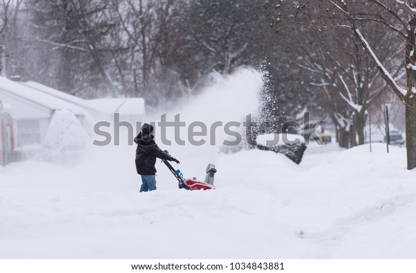 Woman with\
a snow blower cleans a driveway in\
winter