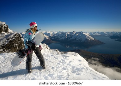 Woman With Snowboard Standing On Top Of Snowy Mountain