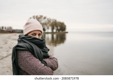 Woman snuggling down into a warm winter scarf on a beach on a cold bleak winter day looking over the woollen textile at the camera with smiling eyes - Shutterstock ID 2085871978