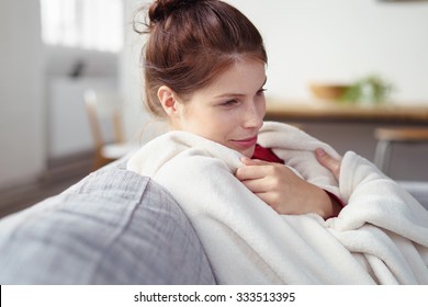 woman snuggling into a warm blanket while sitting on her sofa with a dreamy smile