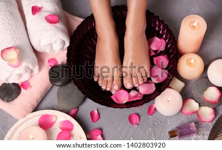 Woman soaking her feet in bowl with water and rose petals on floor, top view. Spa treatment