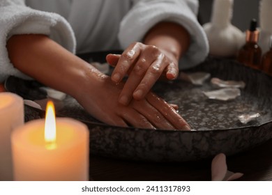 Woman soaking her hands in bowl of water and flower petals, closeup. Spa treatment