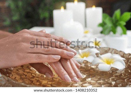 Woman soaking her hands in bowl of water and flowers, closeup with space for text. Spa treatment