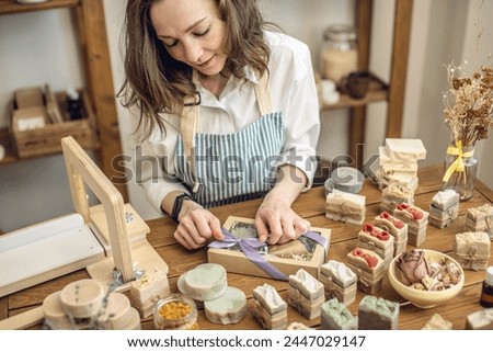 Woman soap maker in a workshop is packing in the gift box handmade natural soap. Cozy creative atmosphere and nice hobby.