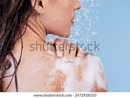 Woman, soap and shower for shoulder in studio, washing and grooming for skincare on blue background. Female person, water and liquid for cosmetics or treatment and hydration for skin, beauty and foam