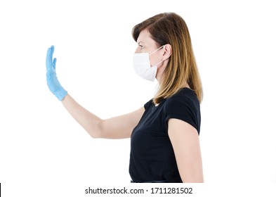 Woman Social Distancing From Corona Virus Covid-19 Wearing A Protective White Face Mask And Medical Gloves Holding Up Hand Saying Stop. Isolated On White Background. Side View Of Young Woman.