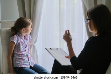 Woman Social Worker Psychologist Talking To Girl Child In Office, Female Counselor Taking Notes In Clipboard. Children Mental Health