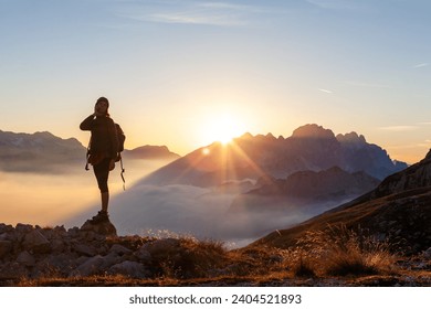 Woman Solo Hiker Talking on her Mobile Device Smart Phone From a Remote Location Above Clouds at Sunset in High Mountains - Powered by Shutterstock