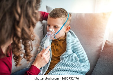 Woman with son doing inhalation with nebulizer at home. Causian little boy making inhalation with nebulizer. Child having respiratory illness helped by mother with inhaler