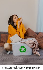 Woman Sorting Old Clothes Into White Container With Recycle Sign. Green Recycling Sign On White Container. Woman Throwing Out Old Clothes.