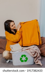 Woman Sorting Old Clothes Into White Container With Recycle Sign. Green Recycling Sign On White Container. Woman Throwing Out Old Clothes.