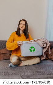 Woman Sorting Old Clothes Into White Container With Recycle Sign. Green Recycling Sign On White Container. Woman Throwing Out Old Clothes.