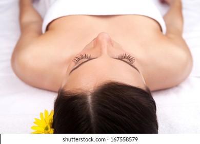 Woman at spa. Top view of beautiful young woman with flower in head lying down and keeping eyes closed