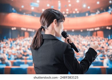 Woman speaking at a microphone in front of a large crowd - Powered by Shutterstock