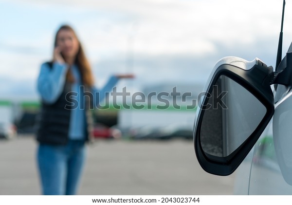 The woman speaks on a cell phone. Traffic\
accident with a car, broken off side rear-view mirror. Driver calls\
the insurance company. Transport damage at parking. Crashed after\
collision or vandalism.