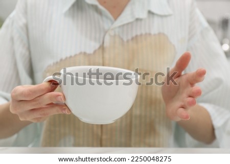 Woman with spilled coffee over her shirt at table, closeup
