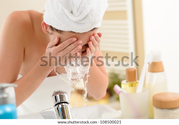 Woman\
splashing face with water above bathroom\
sink