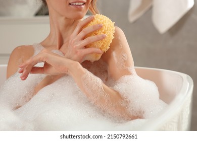 Woman with sponge taking bath indoors, closeup