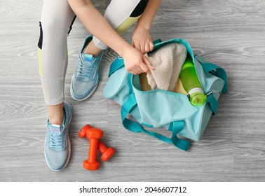 Woman in sport shoes preparing bag for training on light wooden floor - Shutterstock ID 2046607712
