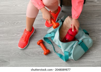 Woman In Sport Shoes Preparing Bag For Training On Light Wooden Background