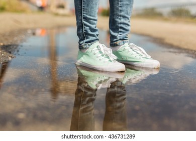 Woman in sport shoes standing in a puddle. Close up shot of foots in a water