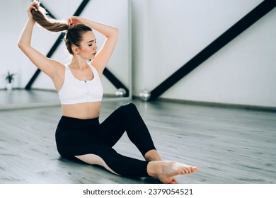Woman in sport top and leggings tying hair in ponytail