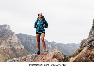 Woman in sports clothes with backpack standing on a rock and looking up during mountain hike - Powered by Shutterstock