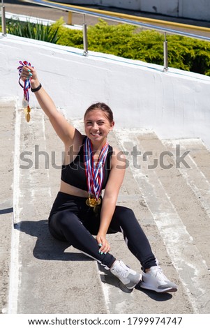 A woman in a sports uniform is sitting on the steps. medals hang on the chest. A woman in a sports uniform sits on the background of the stadium. medals hang on the chest. Victory in the competition.