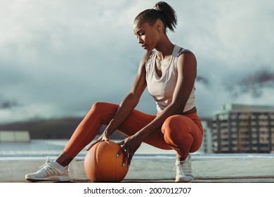 Woman in sportswear with basketball on rooftop. Fitness woman taking a break from workout on building terrace. - Powered by Shutterstock