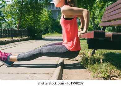 Woman in sportswear doing exercise on triceps on a park bench