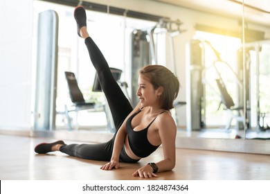 Woman In Sportswear Doing Leg Workout Exercise, Side Leg Lift Raise At Gym.