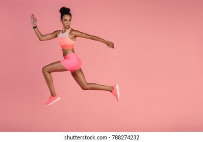 Woman in sportswear running over pink background. Full length shot of healthy young african woman sprinting.