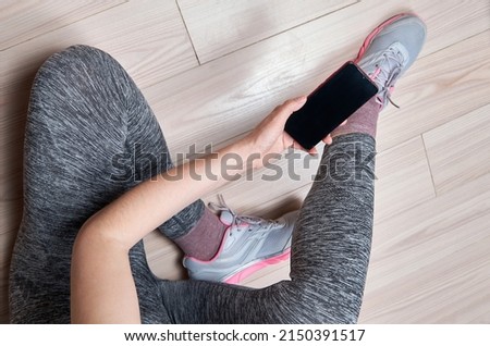 Woman in sportswear and sport shoes with mobile phone sitting on floor, flat lay. Ready for gym workout