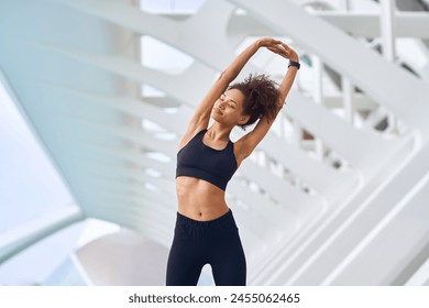 Woman in sportswear stretching arms in front of building - Powered by Shutterstock