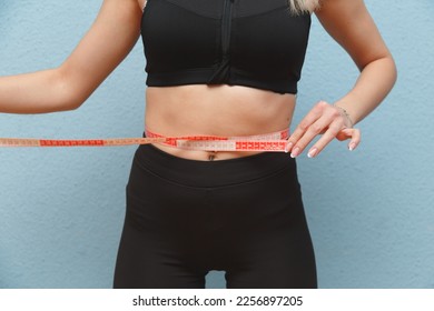 Woman in sportswear taking measurements of her waist, blue background - Shutterstock ID 2256897205