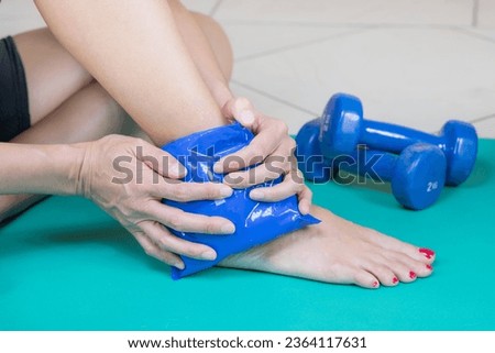 Woman with sportswear using Cold Instant Pack on her left ankle and standing on her fitness mat with weights
