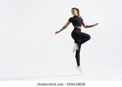 Woman In Sportwear Doing Jump Workout And Look Behind At Empty Space For Logo. Female Athlete With Fit Body Exercising On White Background, Training With Happy Smile.