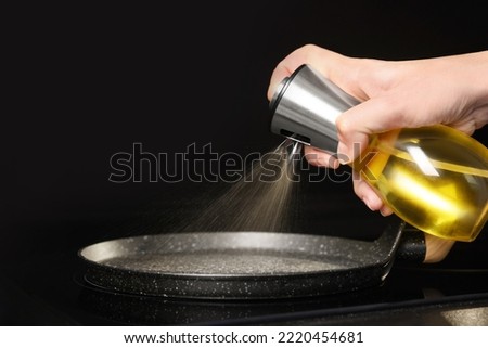 Woman spraying cooking oil onto frying pan on stove, closeup