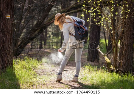 Woman spraying insect repellent against tick at her legs. Protection against mosquito bite during hike in woodland