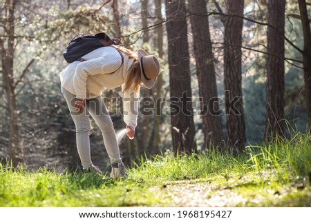Woman spraying insect repellent against tick at her legs. Protection against mosquito bite during hike in forest