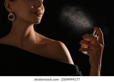 Woman spraying perfume on black background, closeup