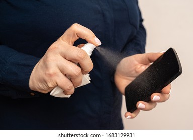 Woman Is Spraying A Smartphone With A Jet Of Aerosol Alcohol Hand Sanitizer To Do Disinfection And Kill Viruses