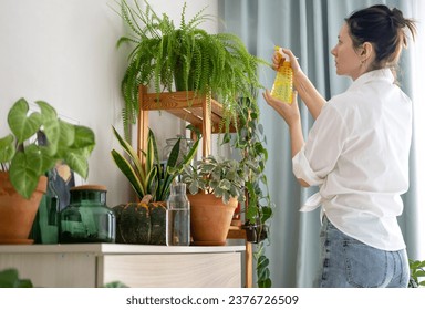 Woman sprays plants in flower pots at home. Indoor gardening. Caring for houseplants home. Interior with lots of plants. - Powered by Shutterstock