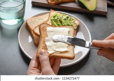 Woman spreading butter on toasted bread at table, closeup
