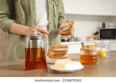 Woman spreading butter onto toasted bread in kitchen - Powered by Shutterstock